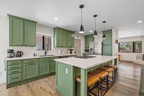 A modern kitchen with green cabinets, a white island with stools, and pendant lighting. - The Getaway in Williams  (Williams)