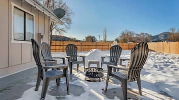 A patio with four chairs and a table, surrounded by snow, with a wooden fence and a satellite dish in the background.