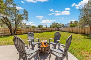 A backyard with a fire pit surrounded by four Adirondack chairs, a wooden fence, and a grassy lawn. - The Getaway in Williams  (Williams)