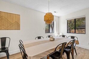 A dining area with a long table, chairs, a hanging light fixture, and a window with a view of trees. - The Getaway in Williams  (Williams)