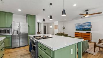 Une cuisine moderne dotée d’un îlot central, d’appareils électroménagers en acier inoxydable et de luminaires suspendus.