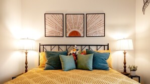 A bed with a patterned bedspread, two side tables with lamps, and three framed artworks on the wall. - The Back Yard-Entire Building Downtown Dog Friendly with Yard (Lake Geneva)