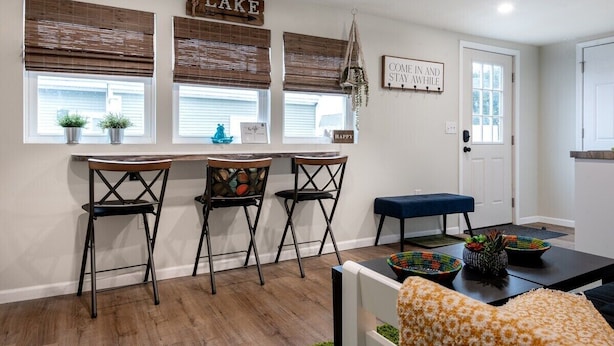 A kitchen with a bar area, three bar stools, a blue bench, and a door with a sign. - The Back Yard-Entire Building Downtown Dog Friendly with Yard (Lake Geneva)