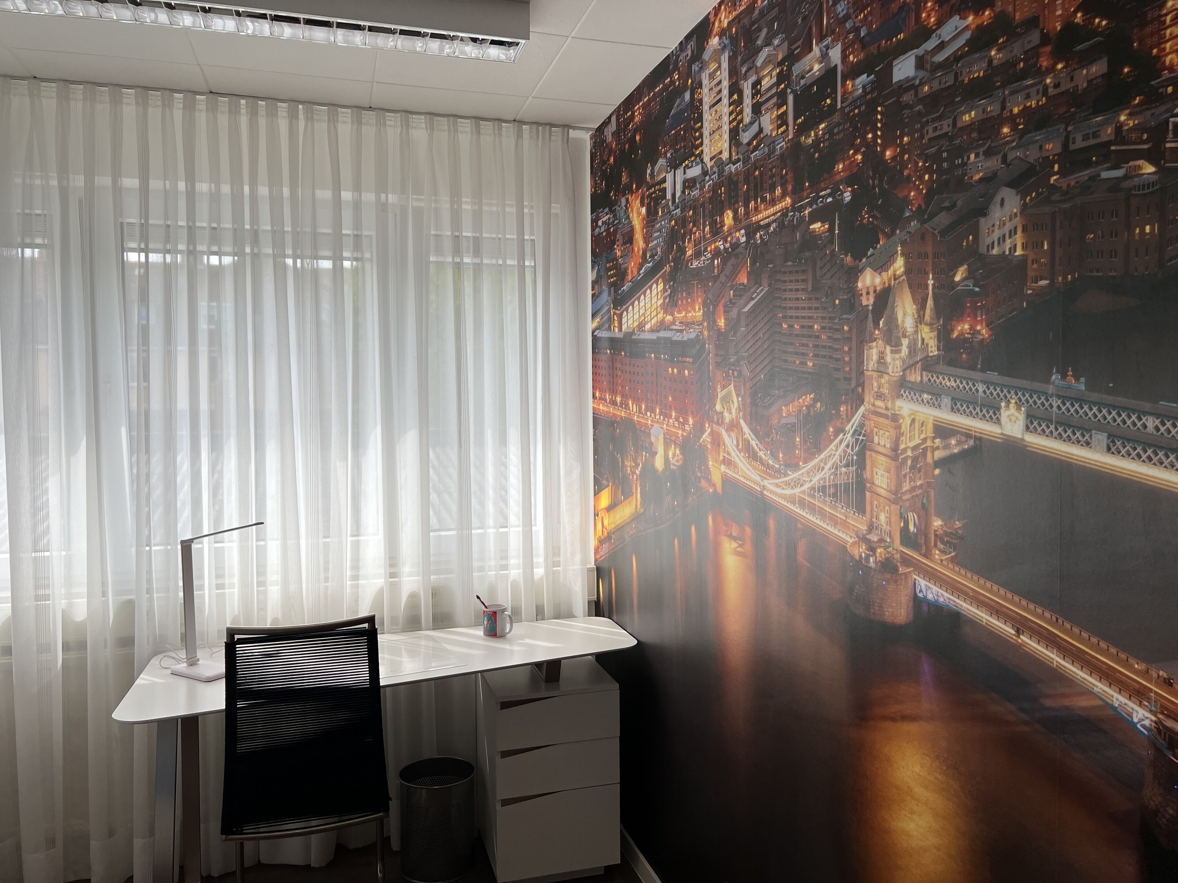 Un moderno spazio ufficio con scrivania, sedia e un'ampia murale raffigurante uno skyline urbano.
