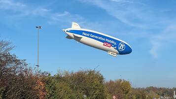 A zeppelin flying over a road with autumn trees and a speed limit sign.