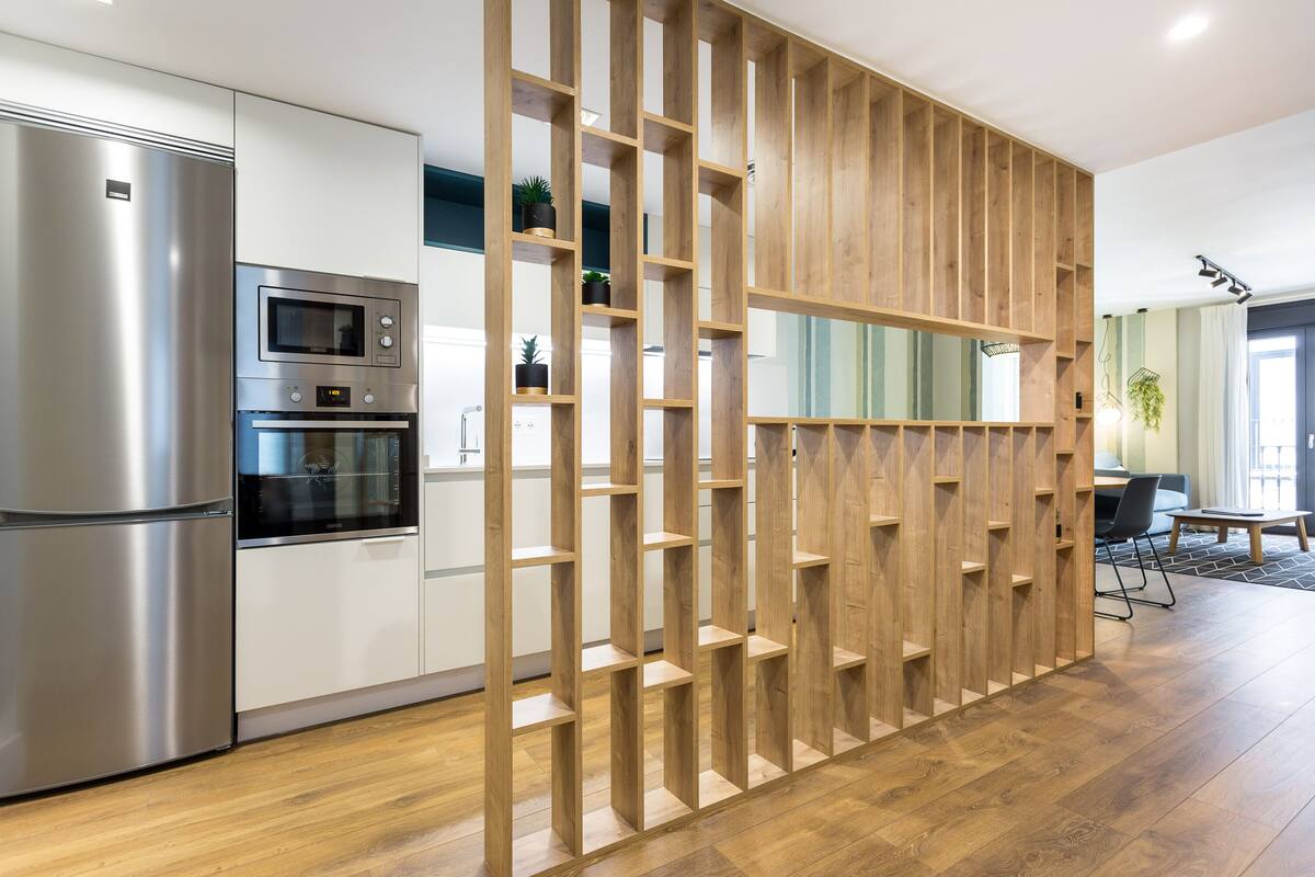 Cozinha moderna com eletrodomésticos de aço inoxidável, prateleiras de madeira e um espaço de refeições com mesa e cadeiras.