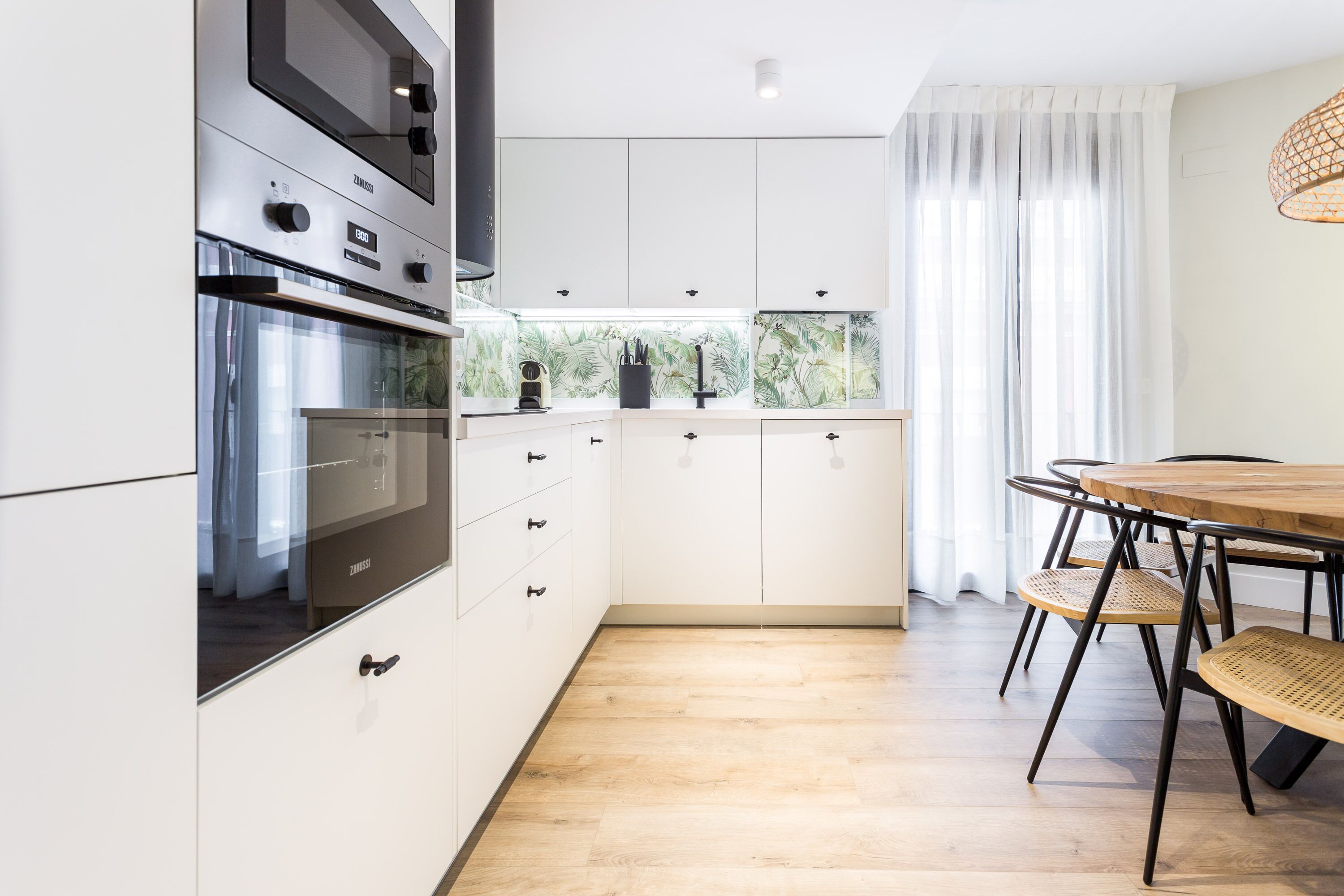 A modern kitchen with white cabinetry, a built-in oven, and a dining area with a wooden table and chairs.