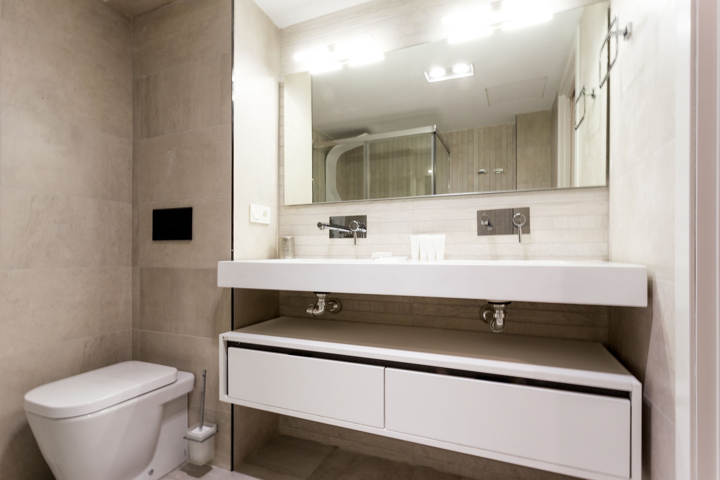 Un baño moderno con inodoro, lavamanos con espejo y cabina de ducha.