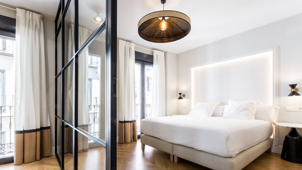 A modern bedroom with a large bed, a glass partition, and a ceiling light fixture. - ELEVEN Apartments Real de la Carretería, by Homing U (Seville)