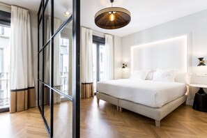 A modern bedroom with a large bed, a glass partition, and a ceiling light fixture. - ELEVEN Apartments Real de la Carretería, by Homing U (Seville)