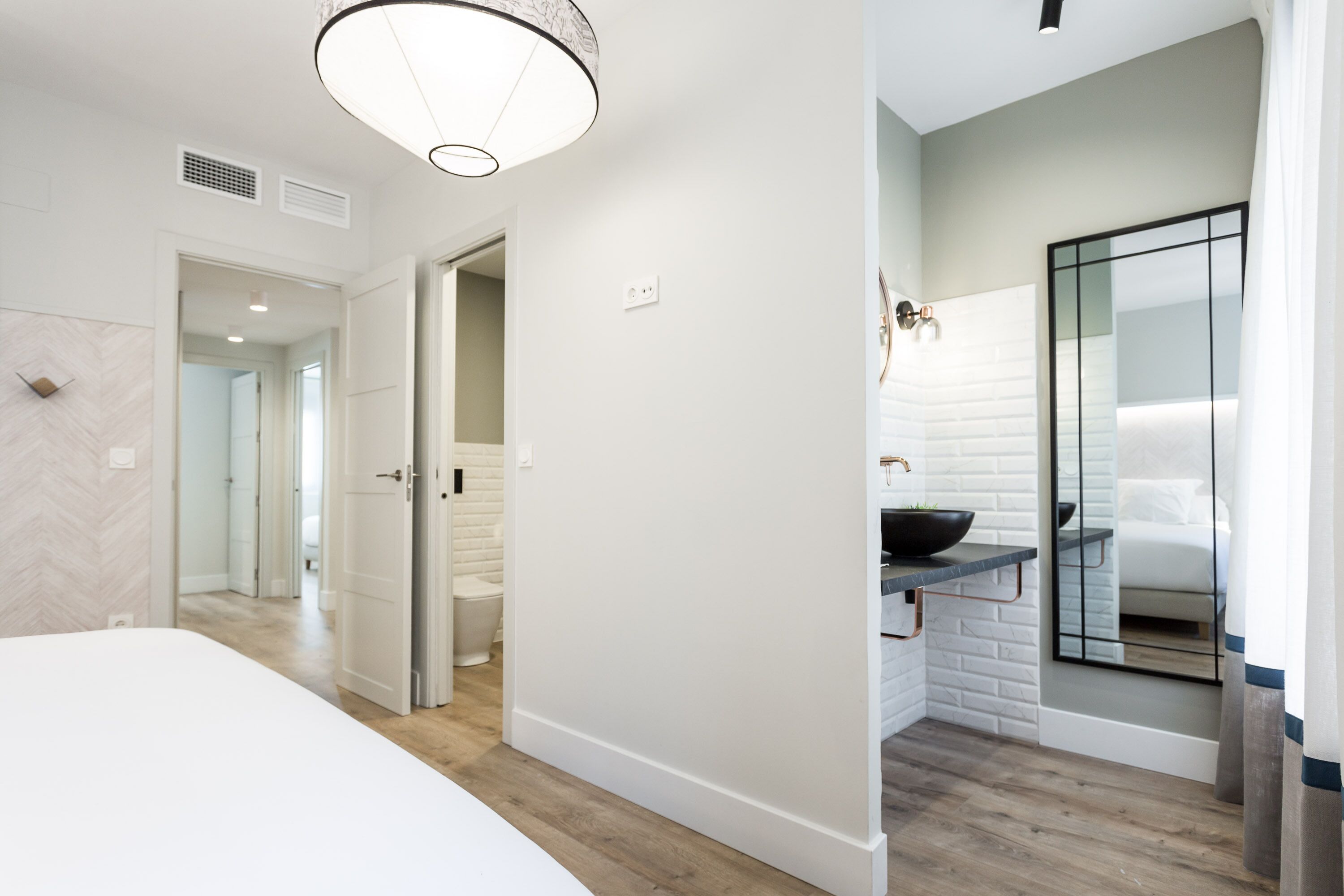 A modern hotel room with a large bed, a bathroom with a black sink, and a mirror.