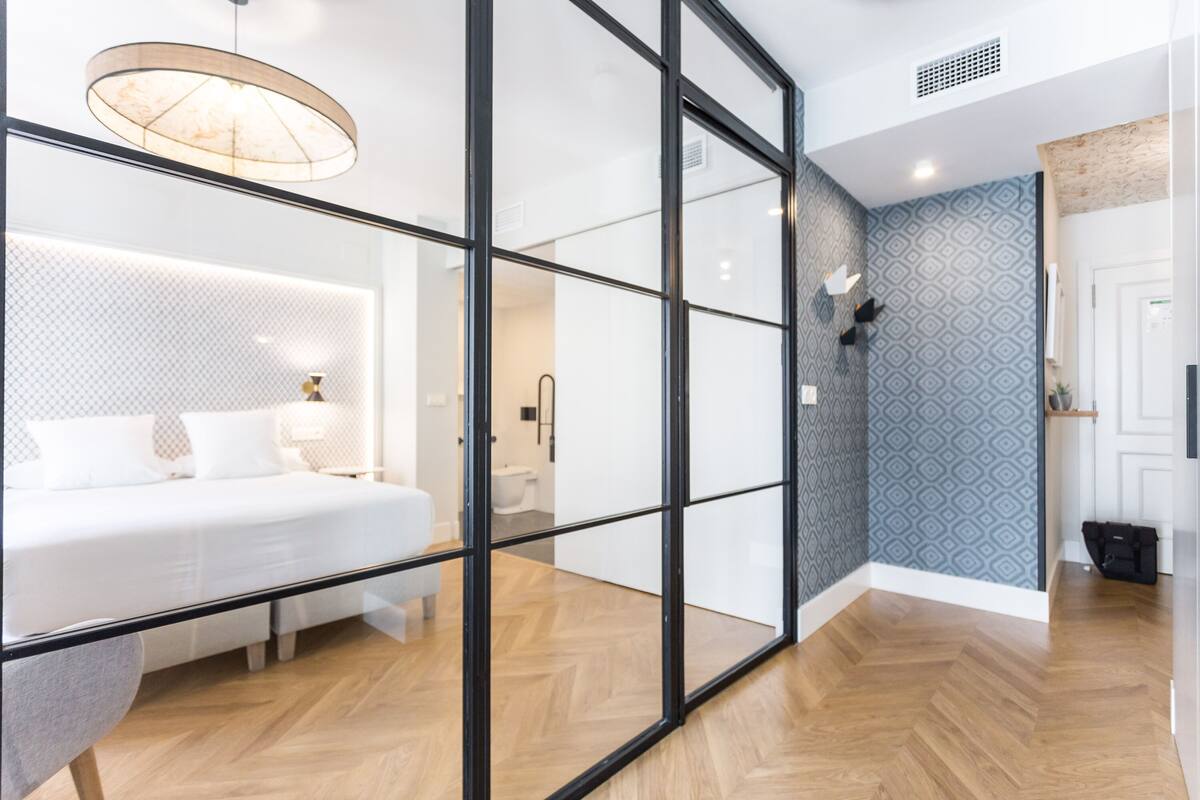 Quarto de hotel moderno com uma cama grande, divisória de vidro, banheiro e parede estampada.