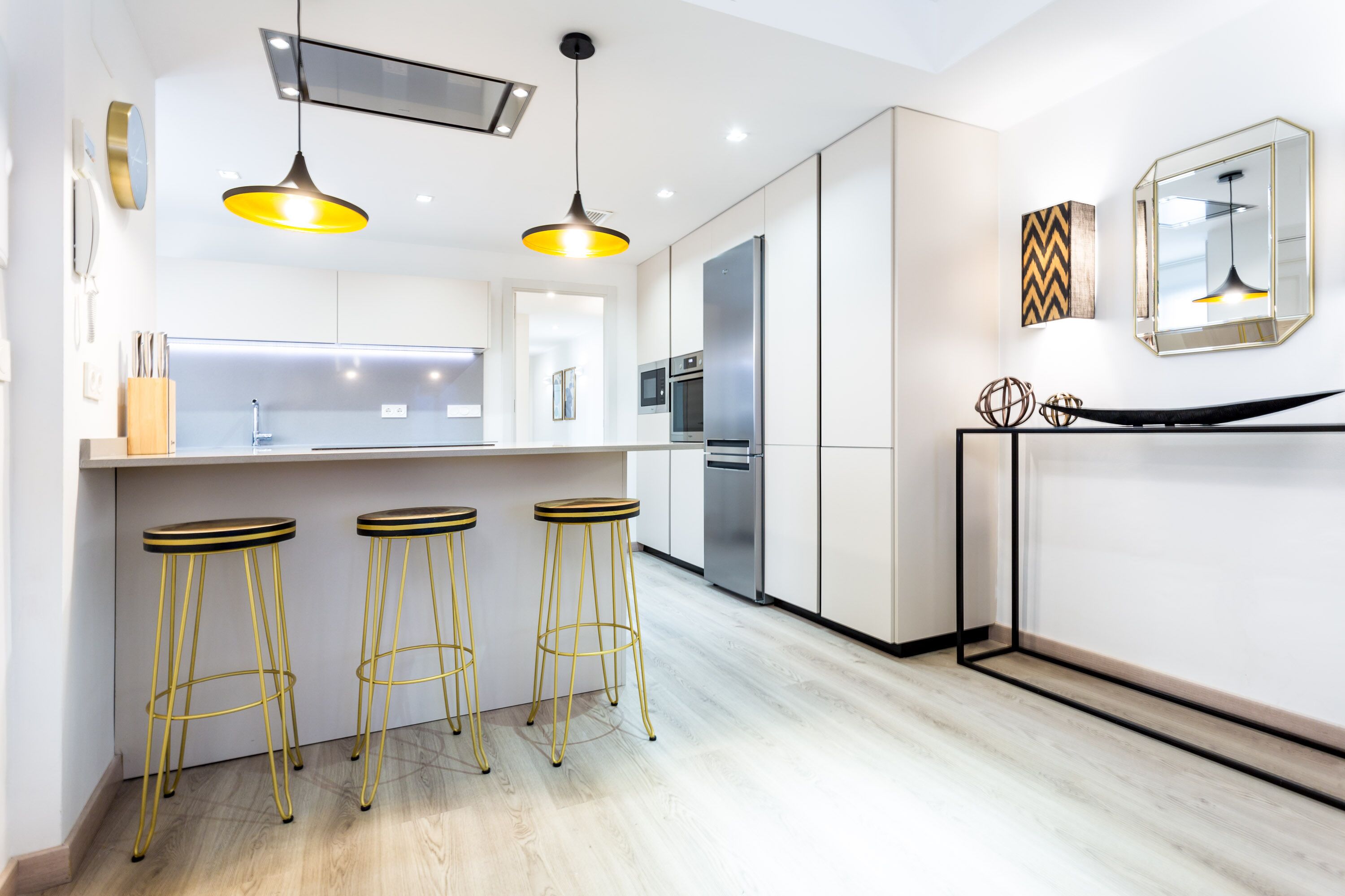 A modern kitchen with a central island, stainless steel appliances, and three yellow bar stools.