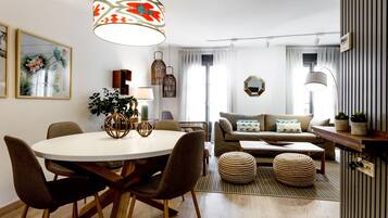 A modern living room with a round dining table, brown chairs, a sofa with cushions, a coffee table, and a hanging light fixture.