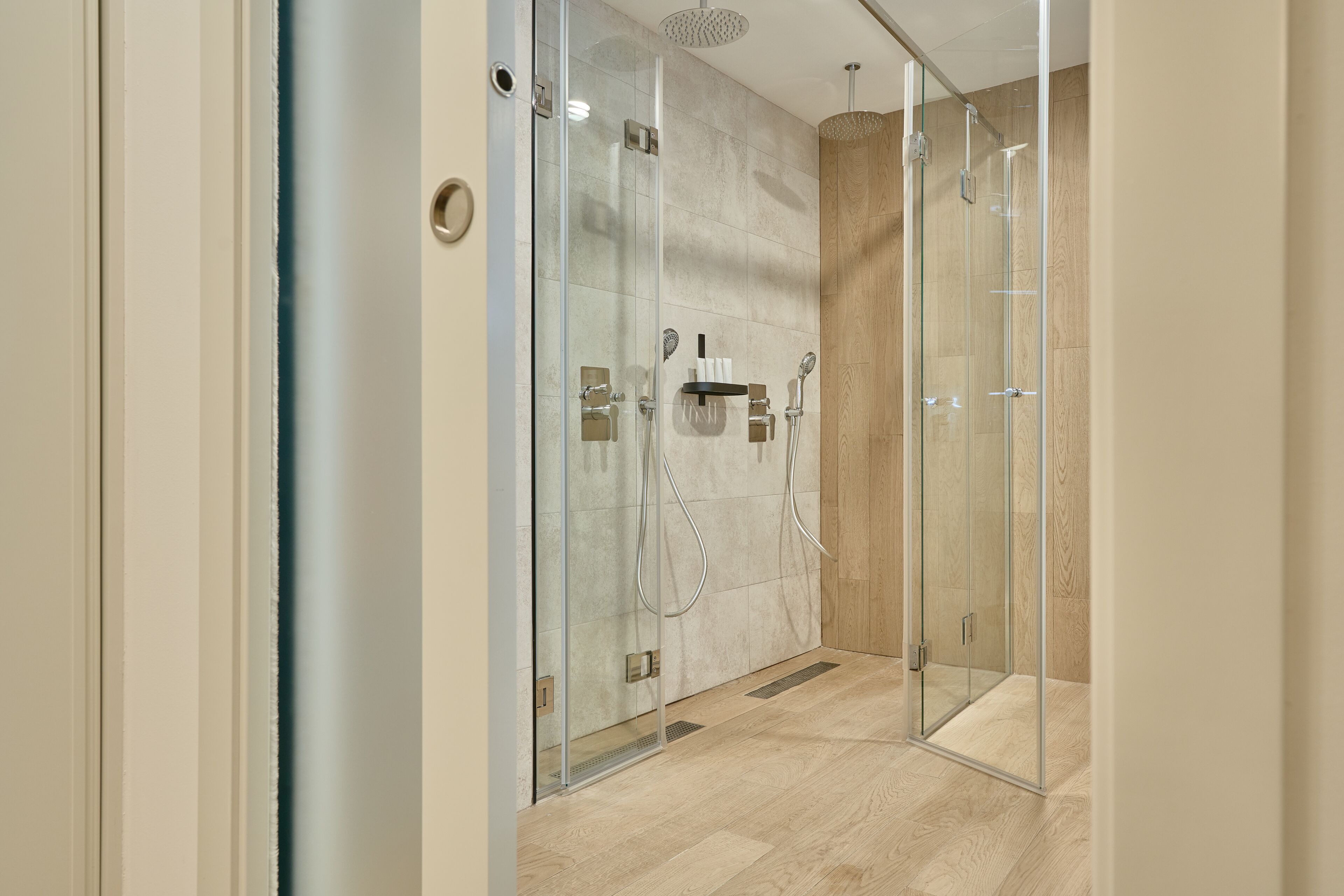 Eine moderne Dusche mit Glastüren, Holzboden und integriertem Ablagebereich mit Handtuch.