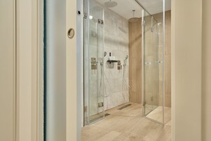 Una ducha moderna con puertas de vidrio, suelo de madera y un estante empotrado con una toalla.
