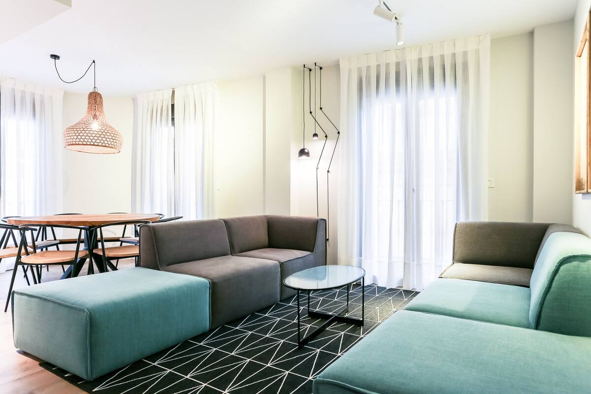 Uma sala moderna com um sofá seccional, uma mesa de centro de vidro e um espaço de jantar com mesa e cadeiras de madeira.