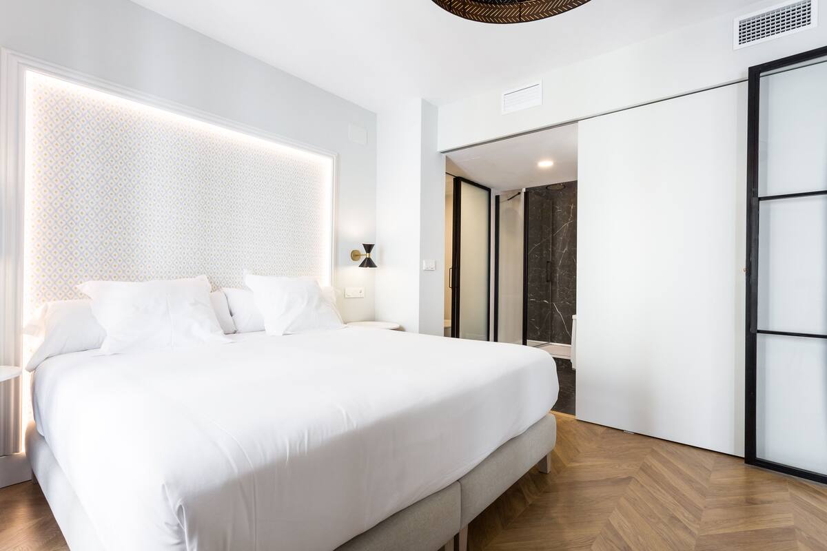 Quarto moderno com uma cama grande, uma mesa de cabeceira, uma luminária na parede e um espelho.