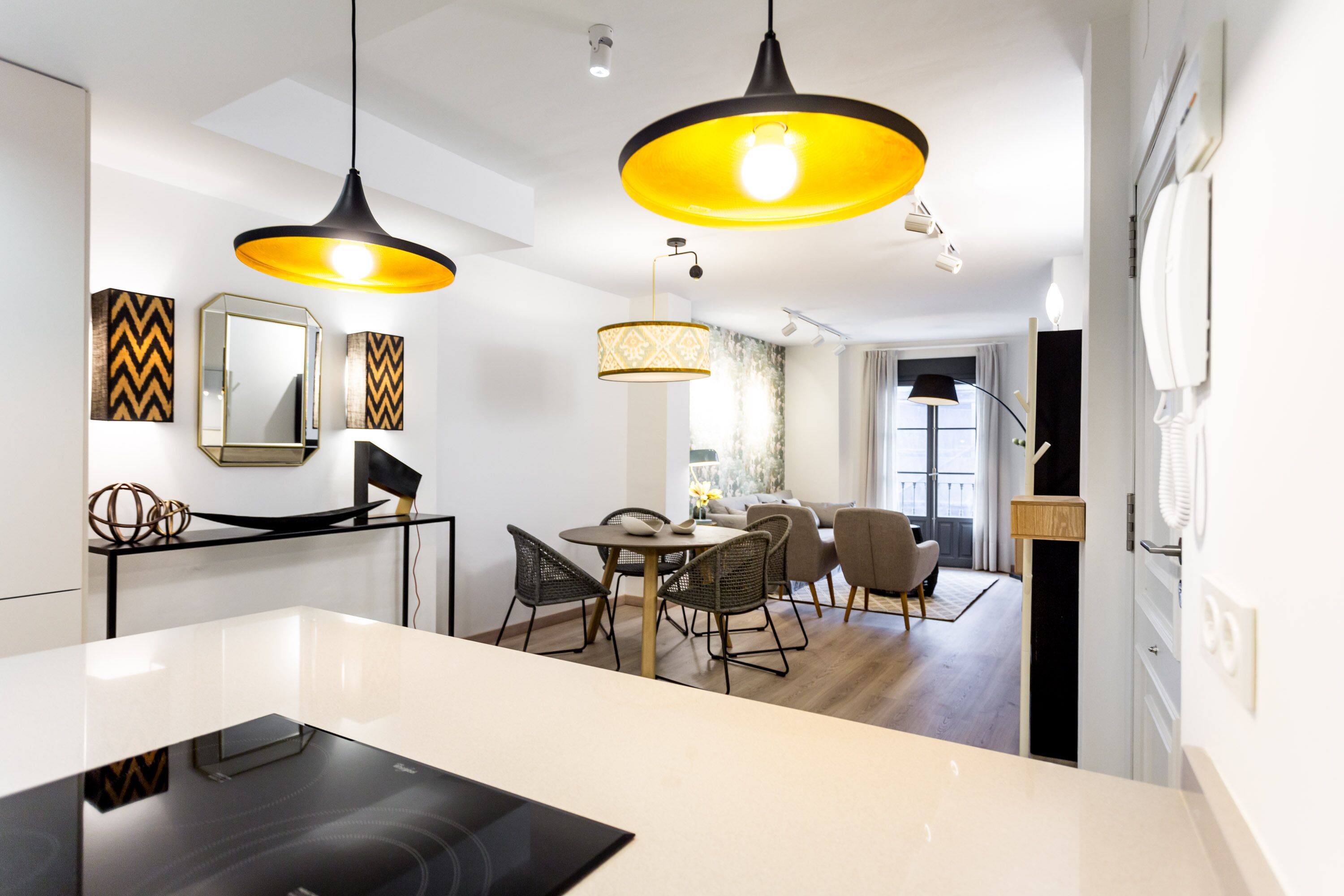 A modern kitchen with a central island, pendant lighting, and a dining area with chairs and a table.