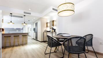 A modern kitchen with a dining area, featuring a round table with chairs, pendant lighting, and a patterned ceiling light.
