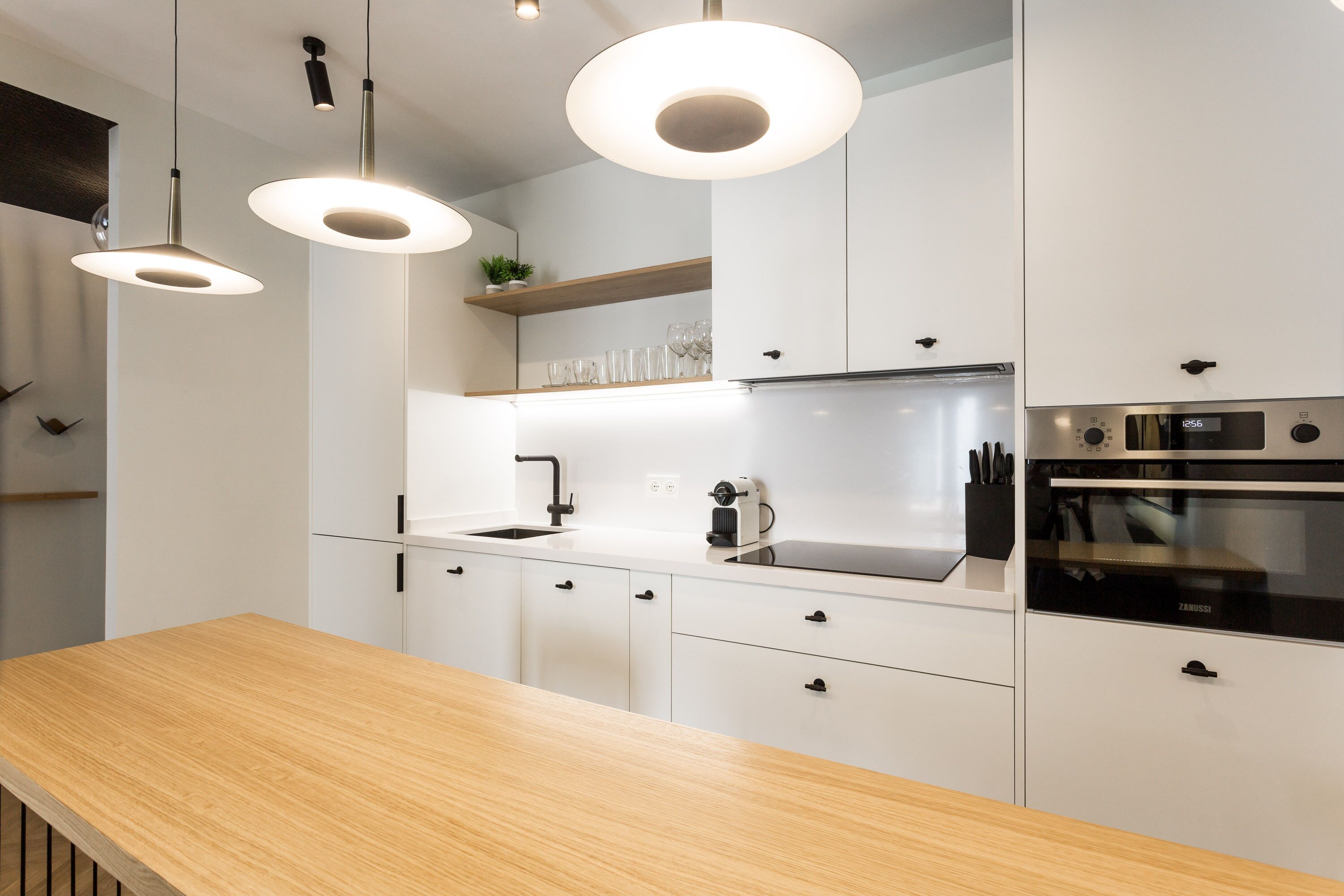 Una cocina moderna con armarios blancos, encimera de madera e iluminación colgante.