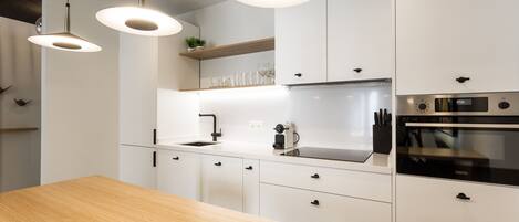 Una cocina moderna con armarios blancos, encimera de madera e iluminación colgante.