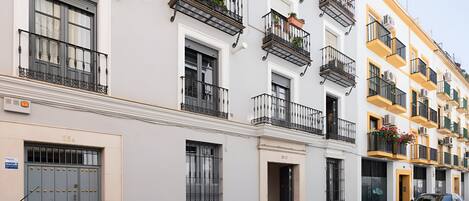 A row of white buildings with balconies, some with plants.