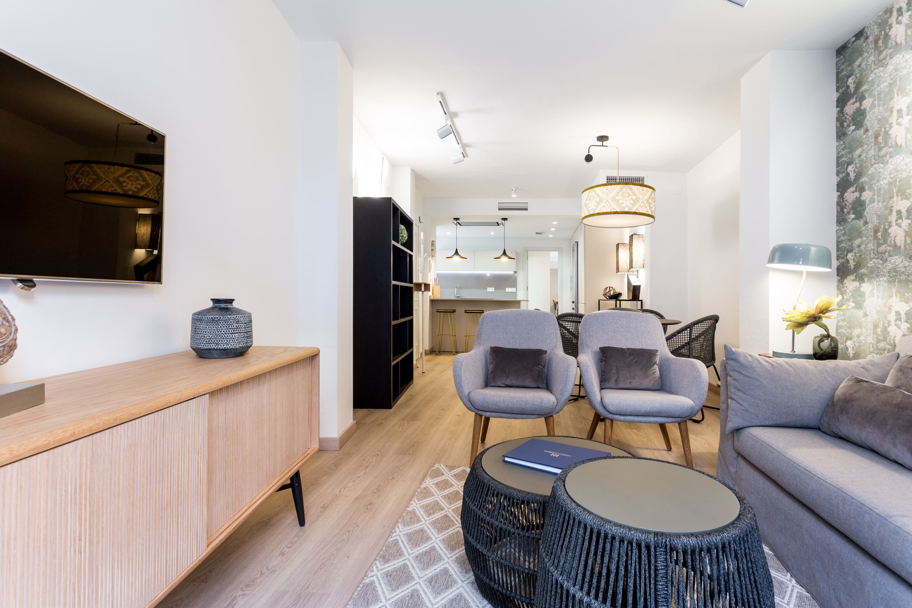 Una sala de estar moderna con un televisor de pantalla plana, una consola de madera, dos sillones grises, un sofá gris y una mesa de centro redonda.