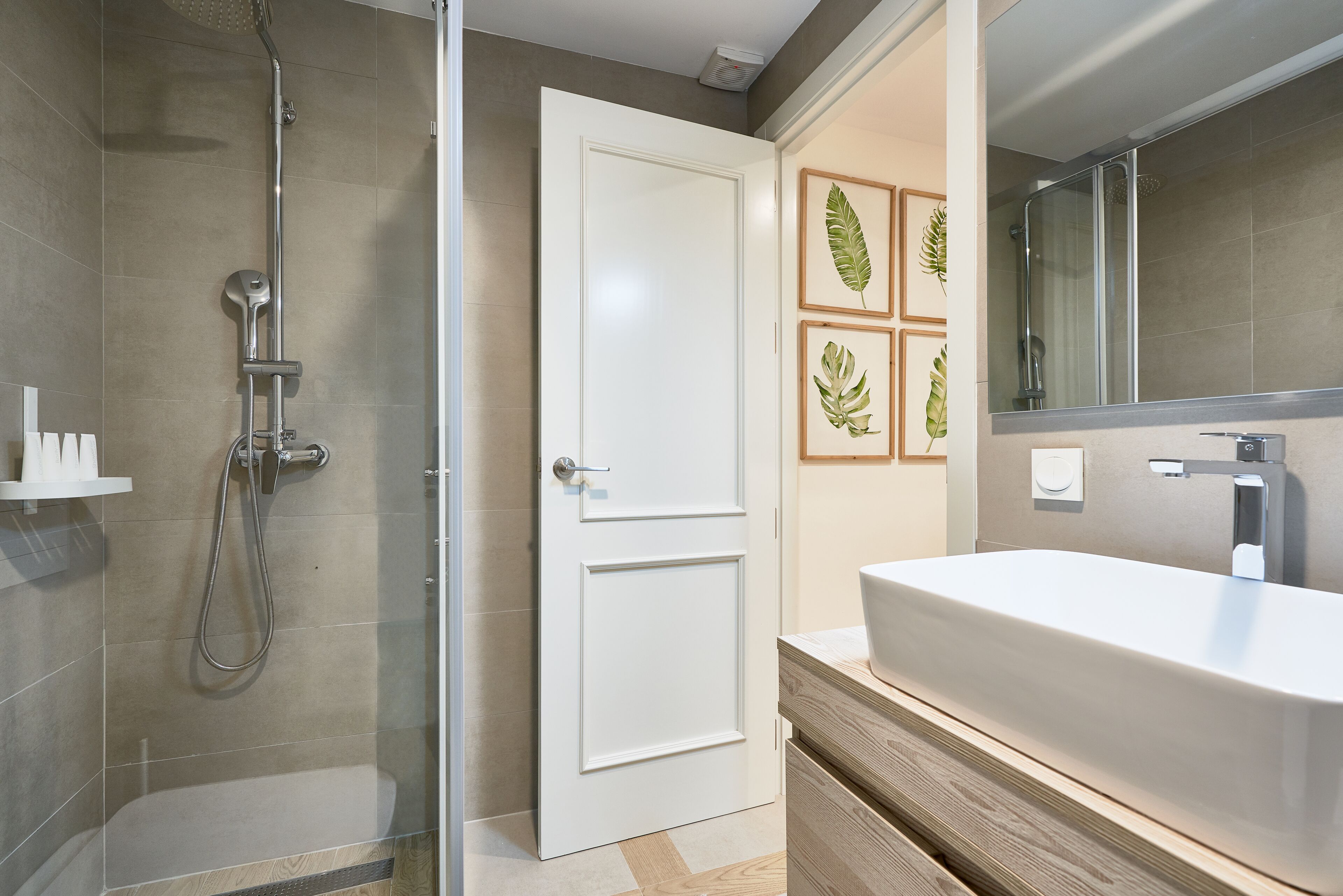Un baño moderno con ducha envuelta en vidrio, un lavabo blanco y un mueble de tocador de madera.
