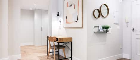 A modern interior with a wooden desk and chair, a framed abstract painting, a mirror, and a small plant on a shelf.