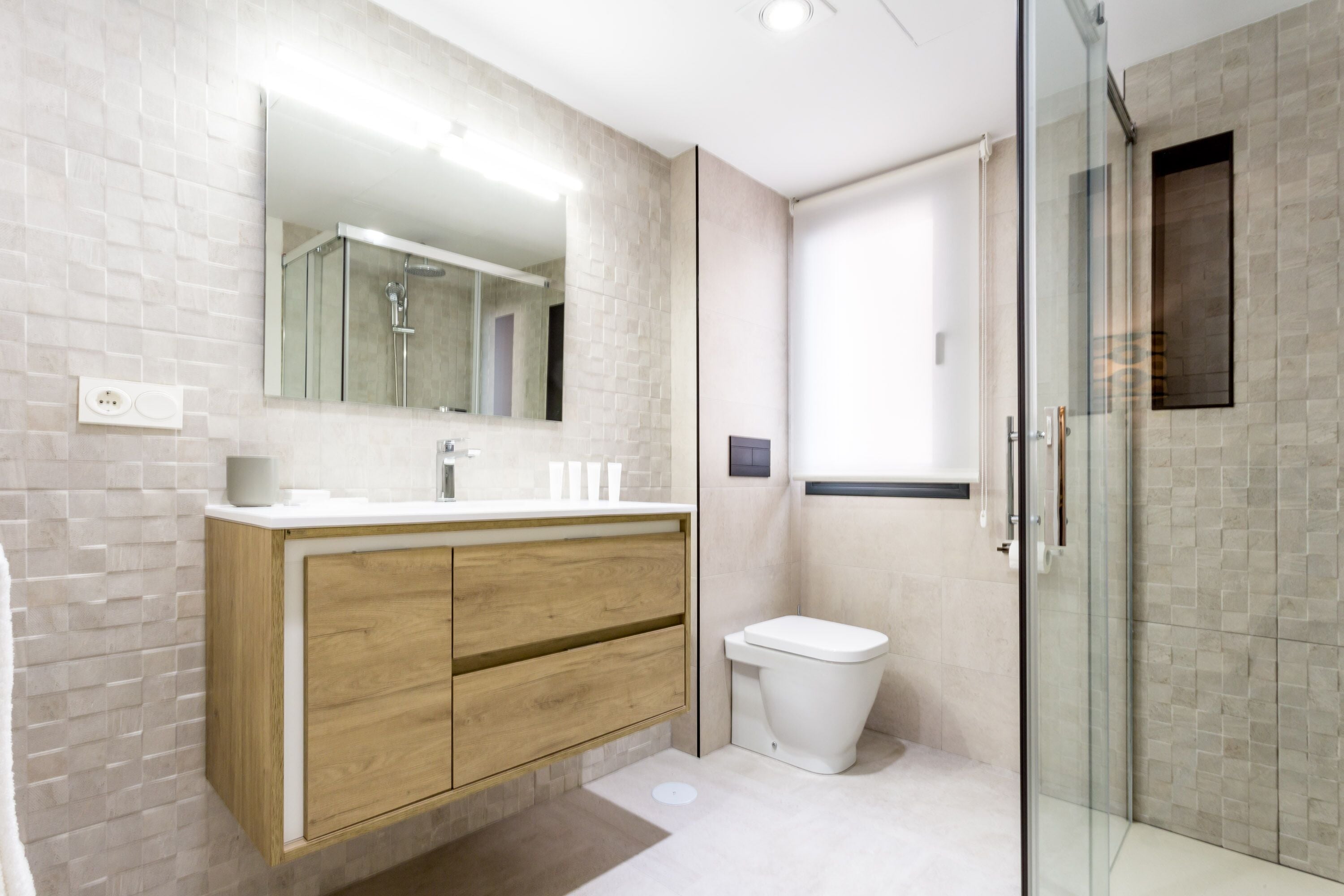 A modern bathroom with a wooden vanity, a glass shower enclosure, and a white toilet.