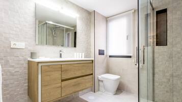 A modern bathroom with a wooden vanity, a glass shower enclosure, and a white toilet.
