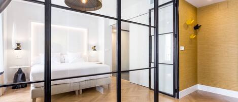 A modern hotel room with a large bed, a glass partition, and a wooden floor.