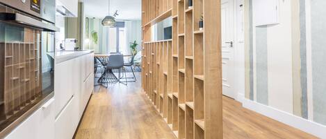 A modern kitchen with built-in appliances, wooden shelving, and a dining area with a table and chairs.