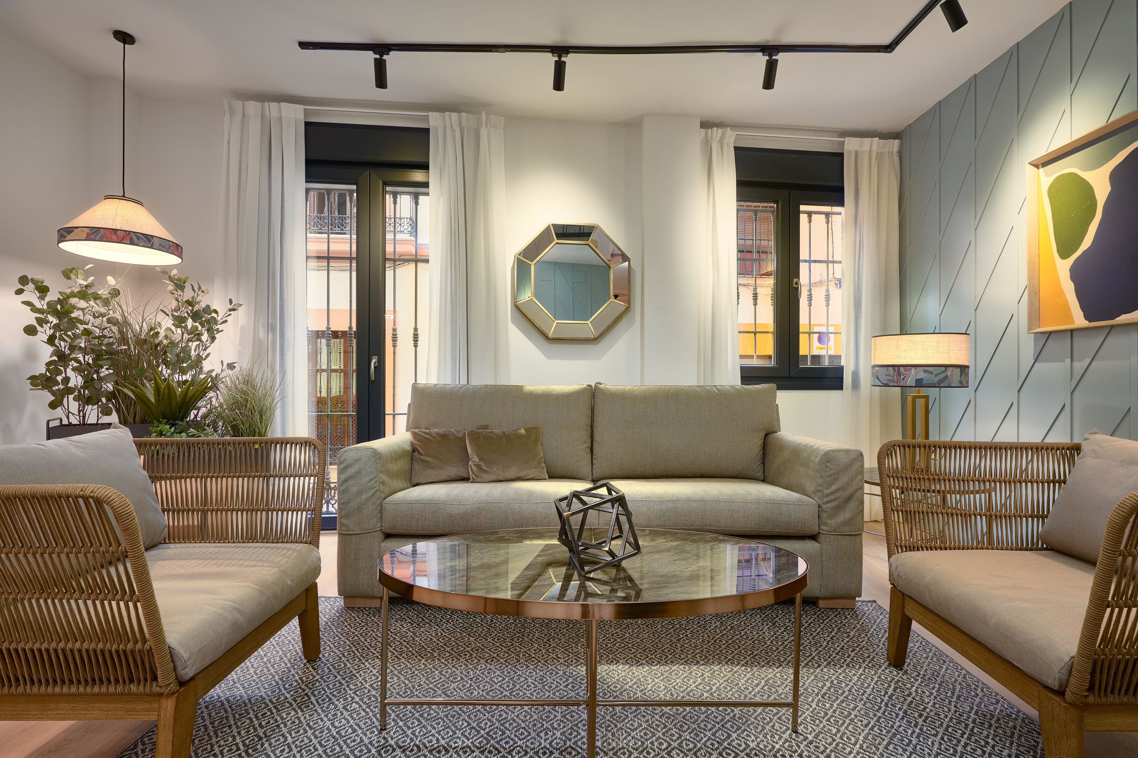 Un salon moderne comprenant un canapé, deux fauteuils en osier, une table basse en verre et une sculpture aux motifs géométriques.