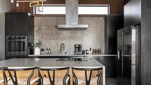 A modern kitchen with a central island, black cabinetry, stainless steel appliances, and a large window above the island.
