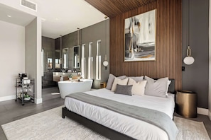 A modern bedroom with a large bed, a bathroom with a bathtub, and a dining area with a table and chairs.