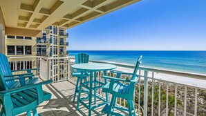 Een balkon met turquoise stoelen en een tafel met uitzicht op een strand.