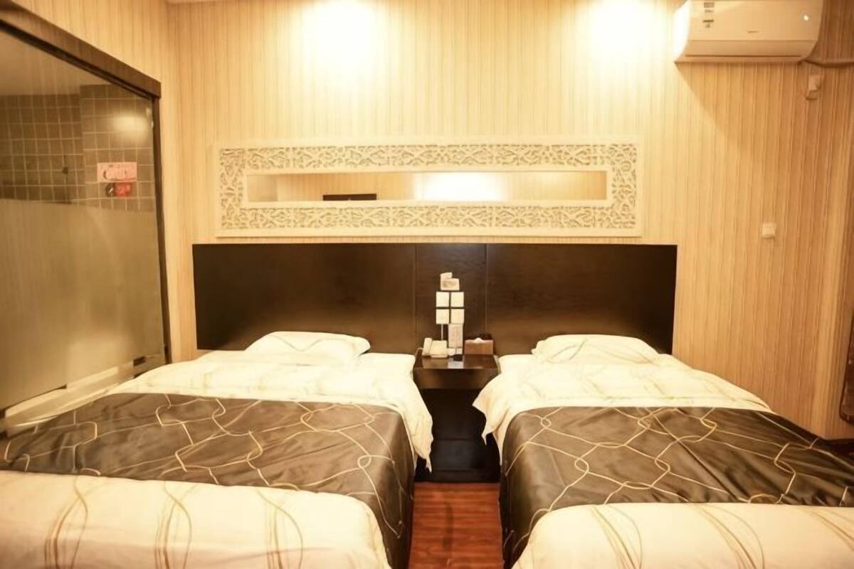 A hotel room with two beds, a small table with toiletries, a mirror above the bed, and a wall-mounted air conditioner.