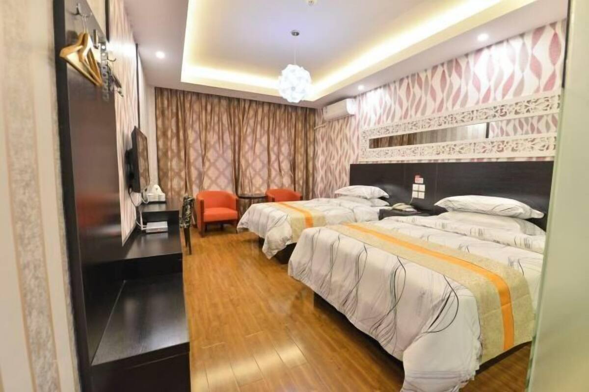 A hotel room with two beds, a TV, a chair, and a wooden floor.