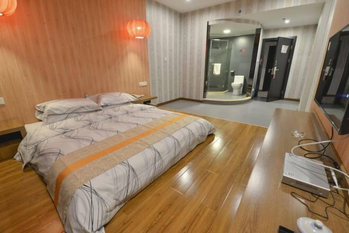 A hotel room with a bed, a desk with a computer, a mirror, and a bathroom visible through a glass door.