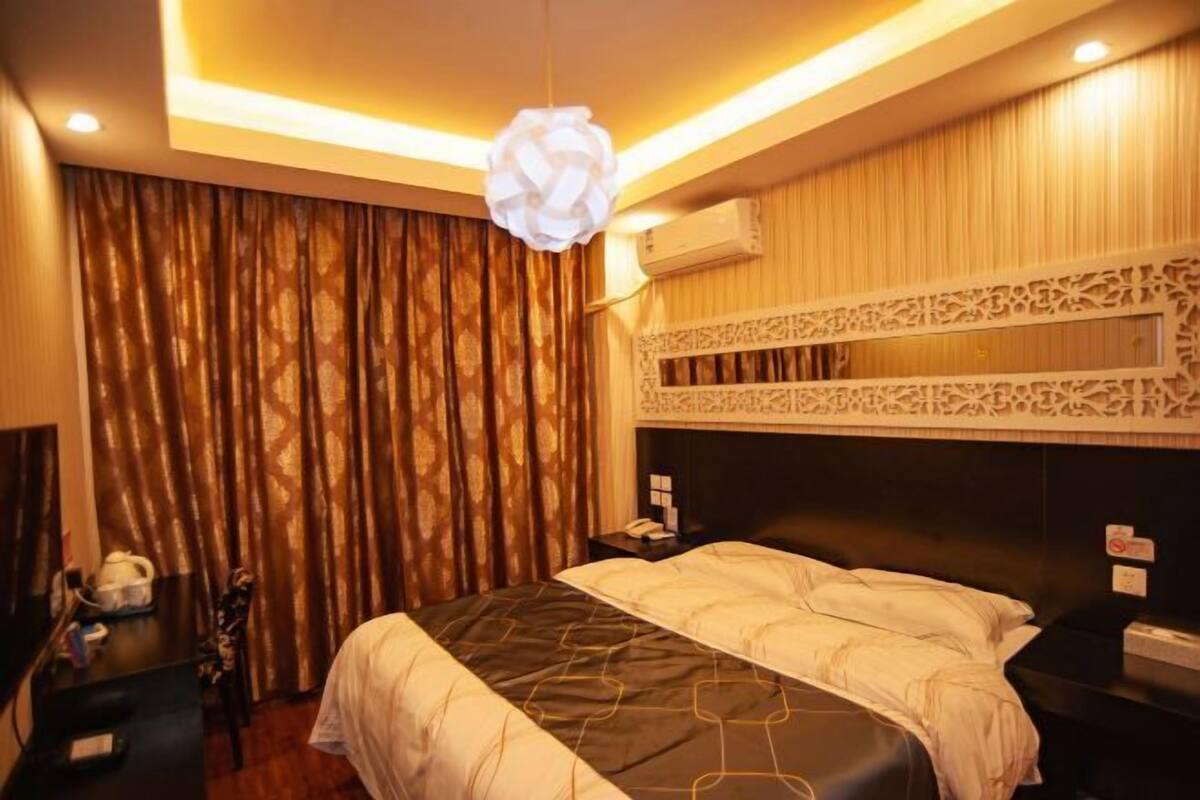 A hotel room with a bed, a desk, a telephone, and an air conditioning unit.