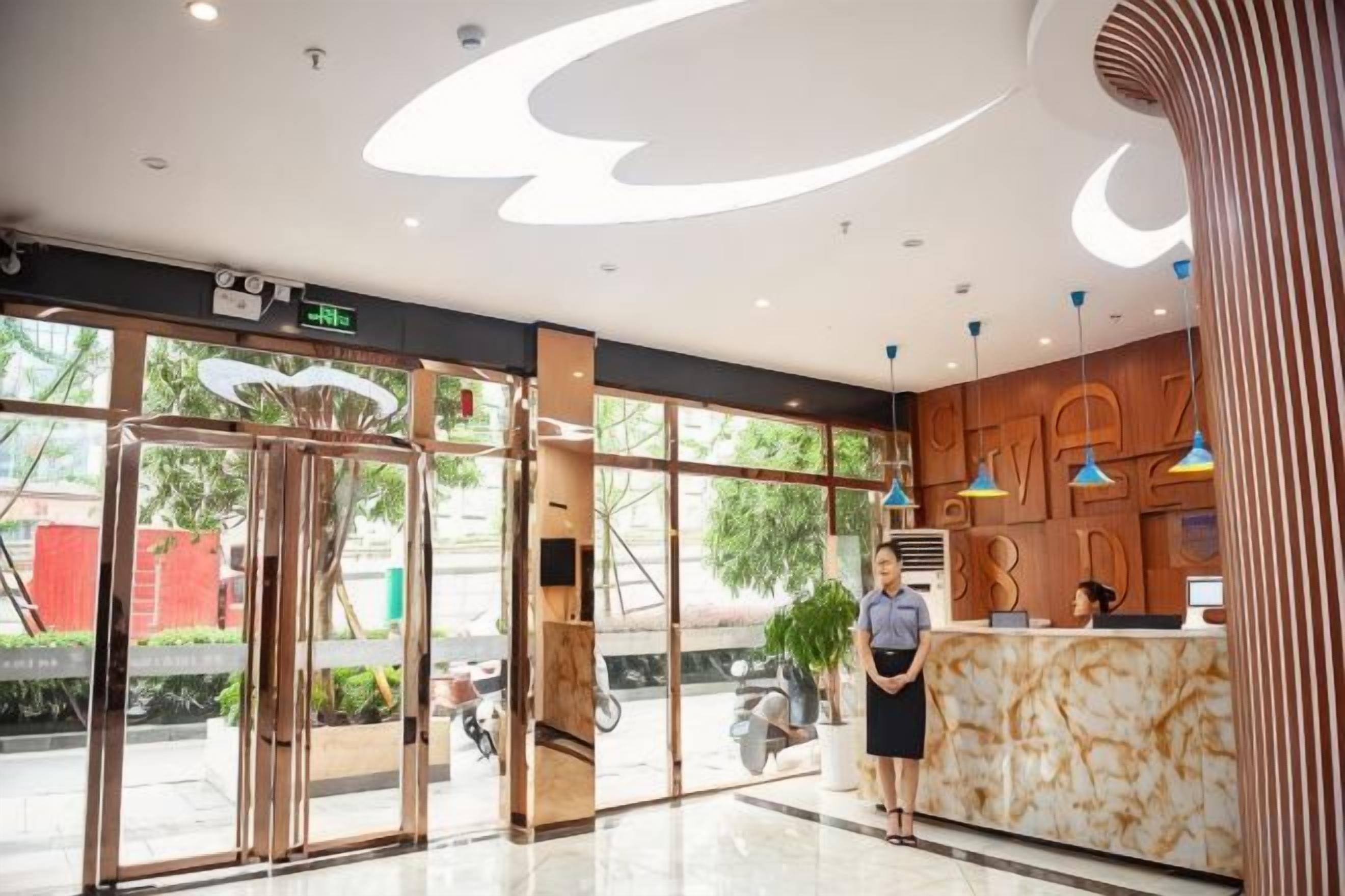A hotel reception area with a marble counter, glass doors, and a modern ceiling design.