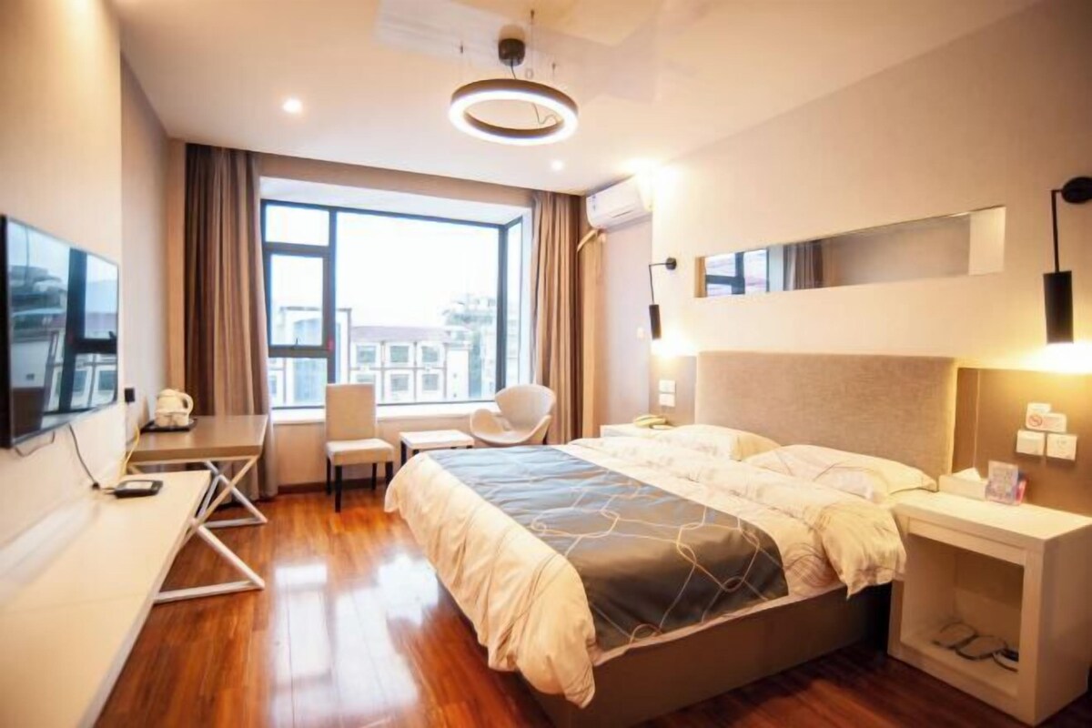 A modern hotel room with a bed, desk, chair, and large window.