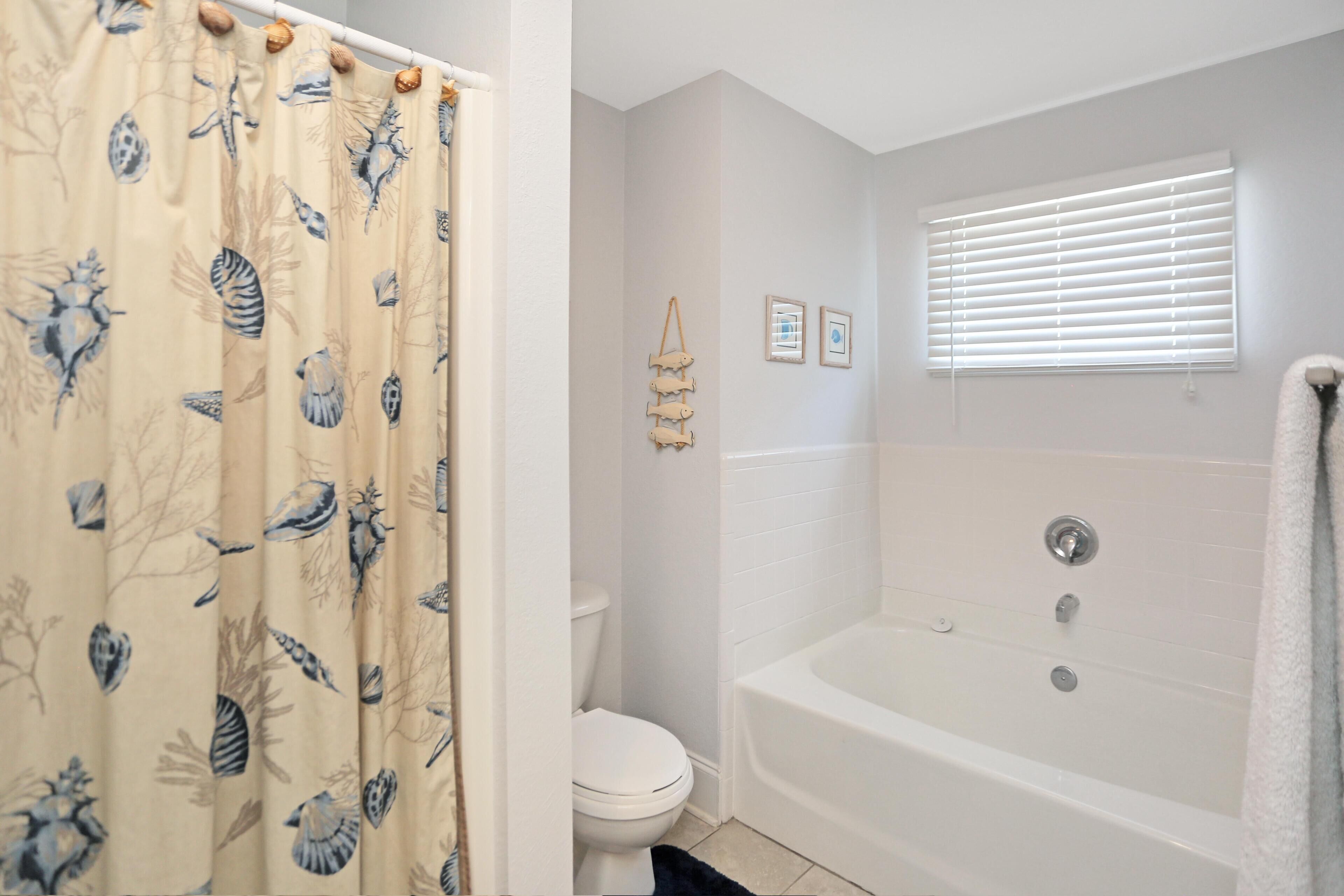 A bathroom with a bathtub, toilet, and shower curtain with a marine life pattern.