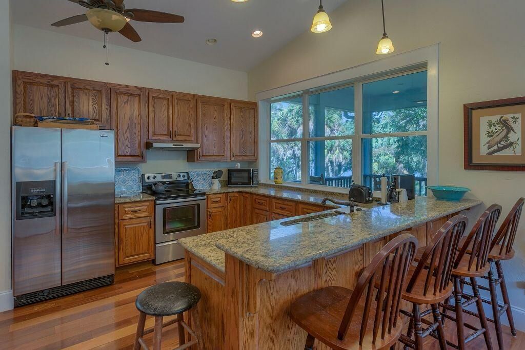 A kitchen with wooden cabinets, stainless steel appliances, a large window, and a bar area with stools.