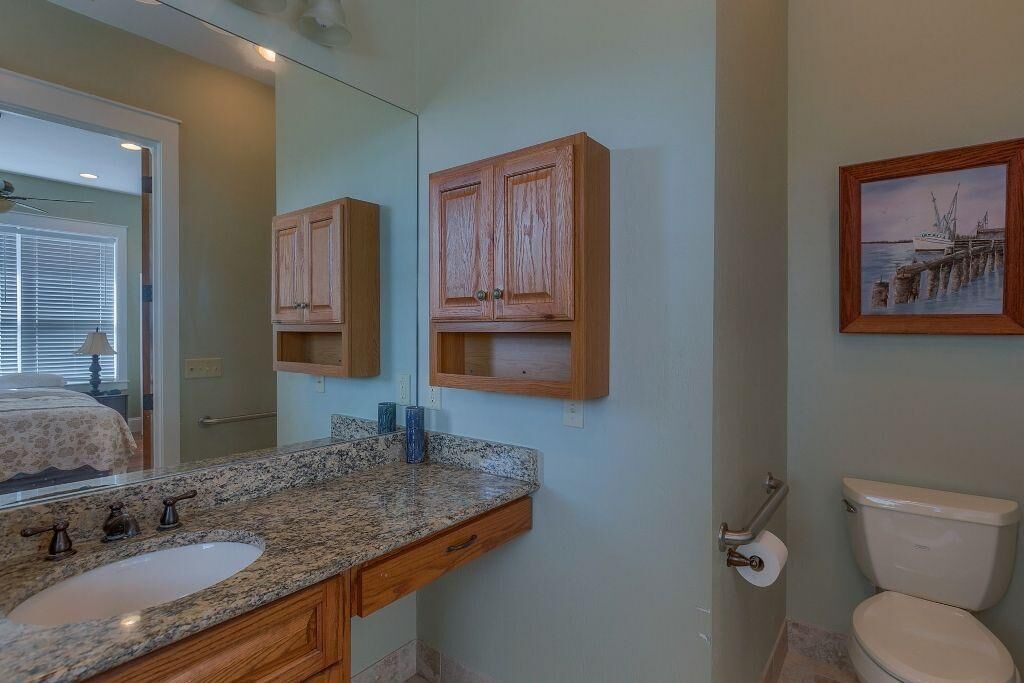 A bathroom with a granite countertop sink, wooden cabinets, a toilet, and a framed picture on the wall.