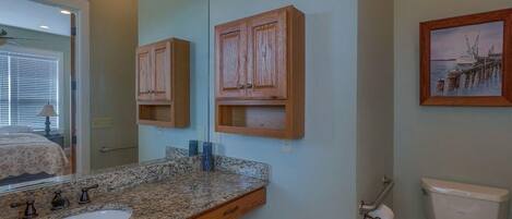 A bathroom with a granite countertop sink, wooden cabinets, a toilet, and a framed picture on the wall.