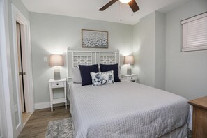 A bedroom with a bed, nightstands, a ceiling fan, and a painting on the wall. - Club at Mexico Beach 1G Red Fish Blue Fish (Port St. Joe)