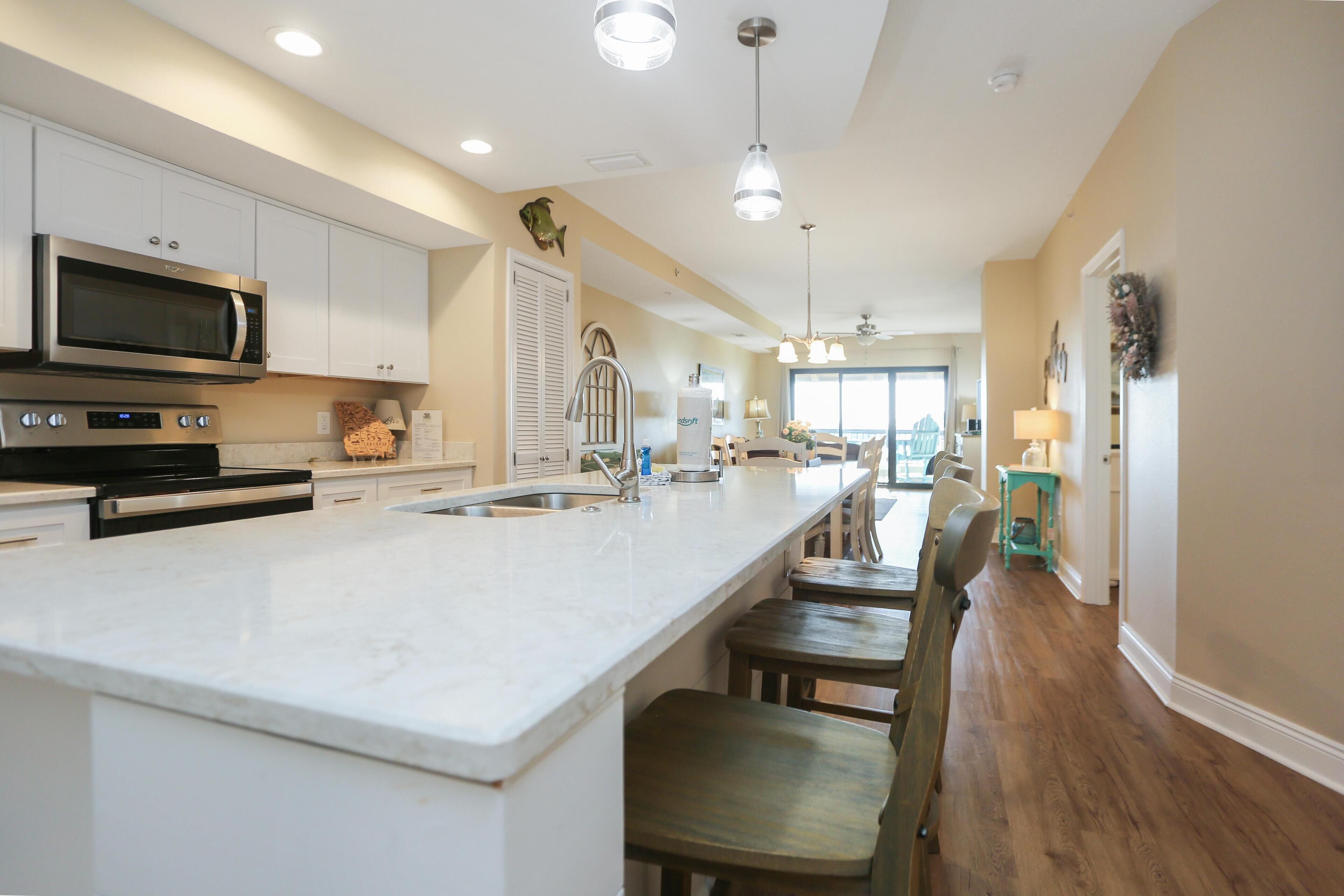 A modern kitchen with white cabinets, a large island, stainless steel appliances, and pendant lighting.